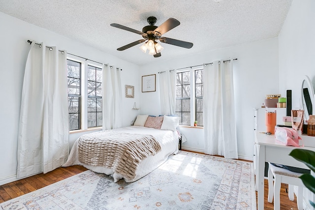 bedroom featuring multiple windows, a textured ceiling, baseboards, and wood finished floors