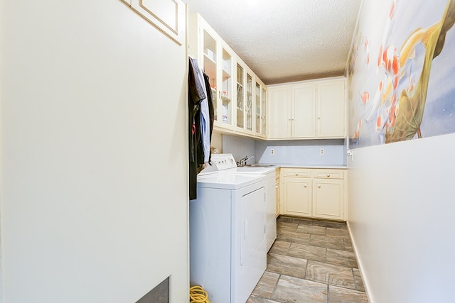 clothes washing area with stone finish flooring, washer and clothes dryer, cabinet space, a textured ceiling, and a sink