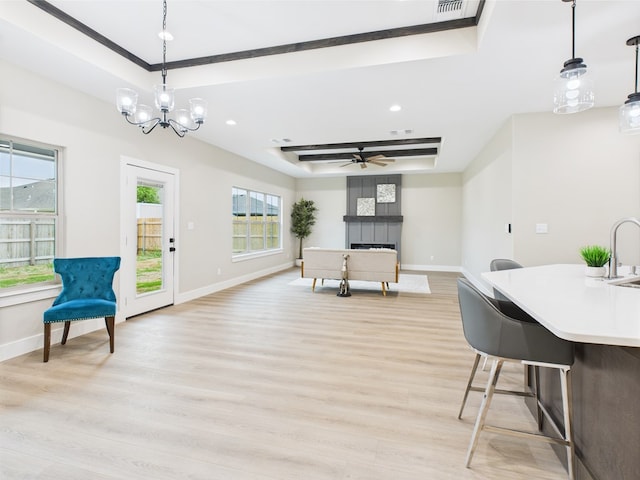 dining room featuring light wood-type flooring, a healthy amount of sunlight, a raised ceiling, baseboards, and a tile fireplace