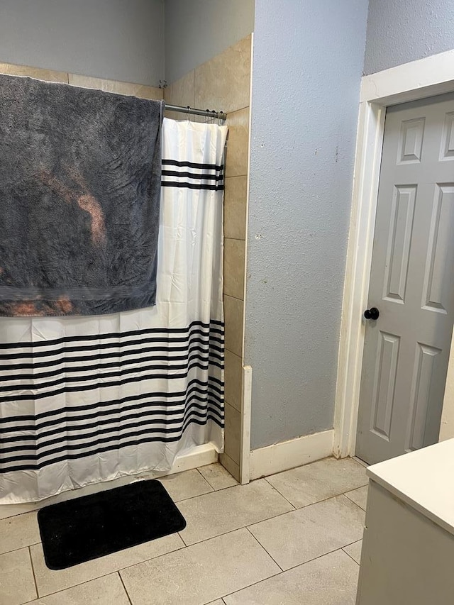 bathroom with tile patterned floors, a shower with shower curtain, baseboards, and a textured wall