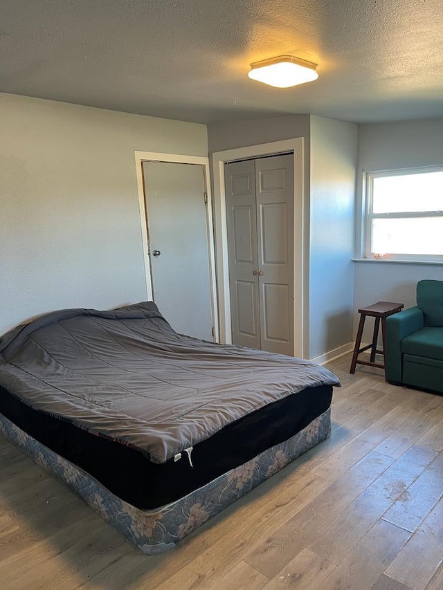 bedroom featuring a closet, a textured ceiling, baseboards, and hardwood / wood-style floors