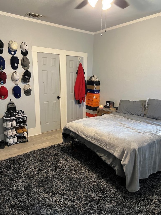 bedroom featuring crown molding, wood finished floors, visible vents, and ceiling fan