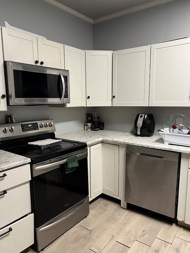 kitchen with white cabinetry, appliances with stainless steel finishes, light wood-type flooring, and crown molding