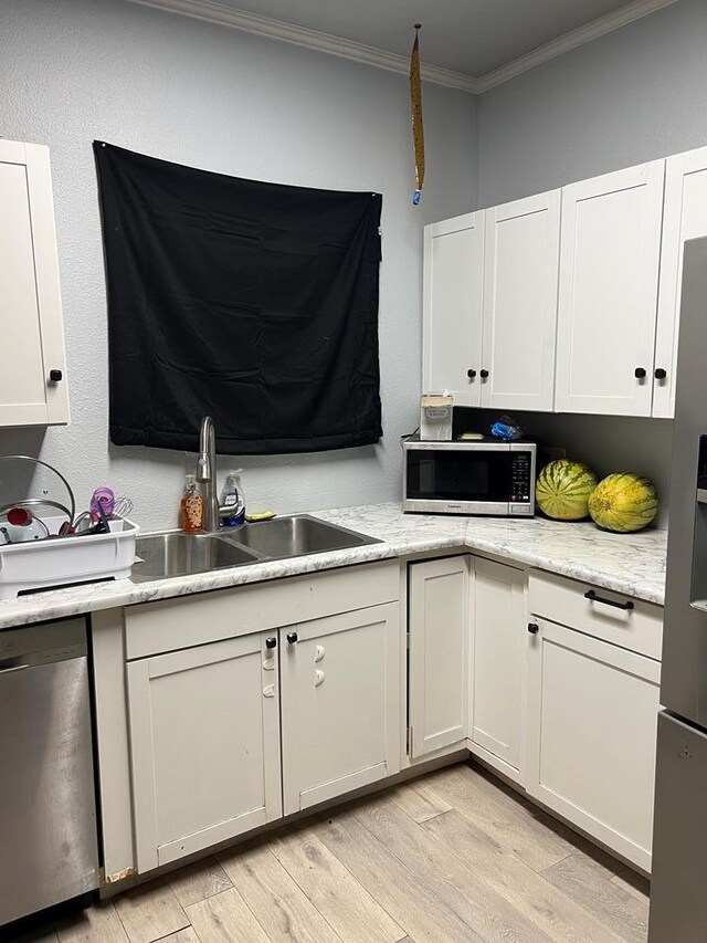 kitchen with a sink, ornamental molding, stainless steel appliances, white cabinetry, and light wood-type flooring