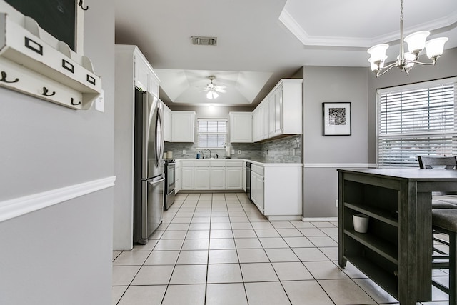 kitchen featuring appliances with stainless steel finishes, white cabinetry, decorative backsplash, hanging light fixtures, and a tray ceiling