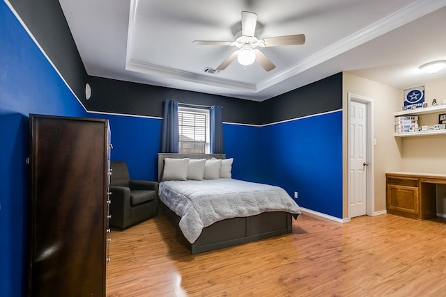 bedroom featuring hardwood / wood-style flooring, ceiling fan, a tray ceiling, built in desk, and ornamental molding