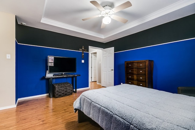 bedroom featuring hardwood / wood-style flooring, ornamental molding, ceiling fan, and a tray ceiling