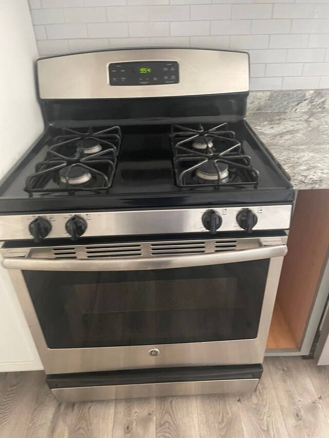 room details featuring stainless steel range with gas cooktop, backsplash, and light hardwood / wood-style flooring