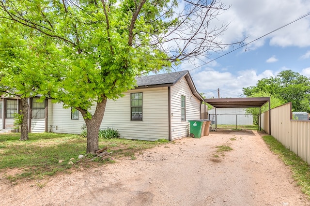 view of side of home featuring a detached carport, a shingled roof, dirt driveway, and fence