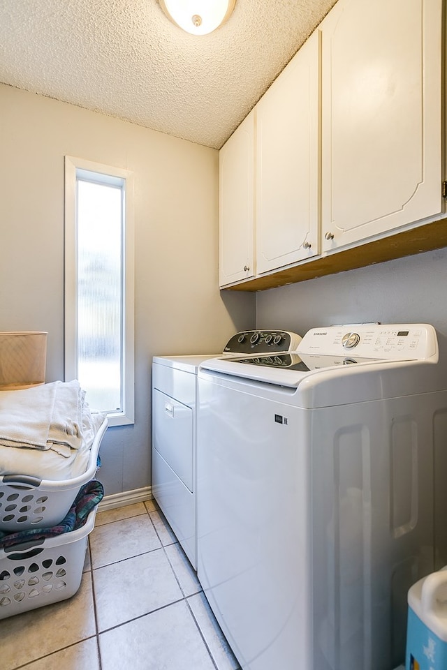 clothes washing area featuring light tile patterned flooring, cabinets, separate washer and dryer, and a textured ceiling