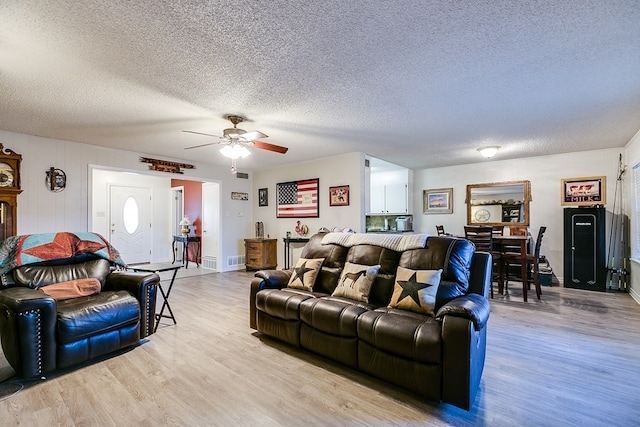 living room featuring ceiling fan, a textured ceiling, and light wood-type flooring