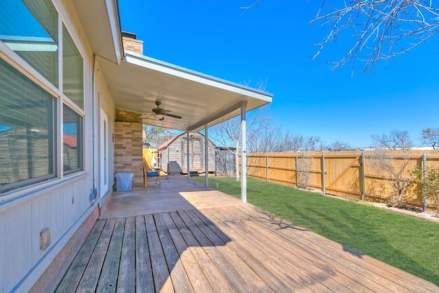 wooden deck with ceiling fan, a shed, a fenced backyard, a yard, and an outbuilding