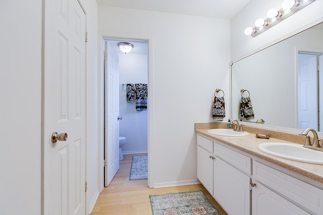 bathroom featuring a sink, toilet, wood finished floors, and double vanity