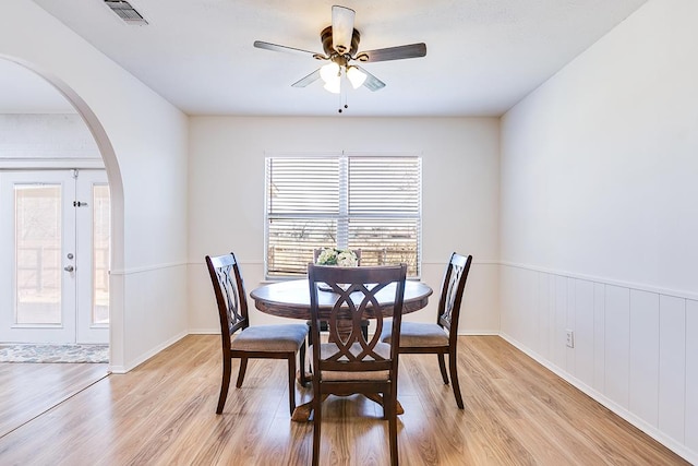 dining room with a ceiling fan, visible vents, arched walkways, light wood-style floors, and wainscoting