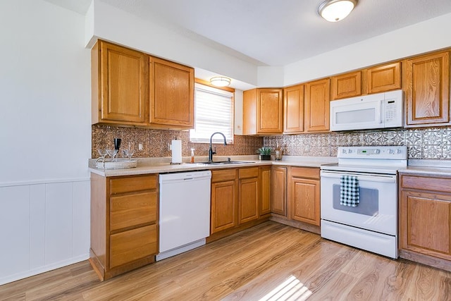 kitchen with a sink, white appliances, light wood-style flooring, and wainscoting