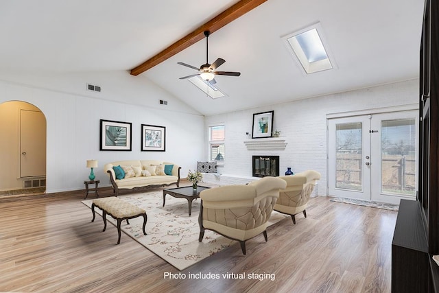 living area featuring visible vents, light wood finished floors, arched walkways, ceiling fan, and lofted ceiling with skylight