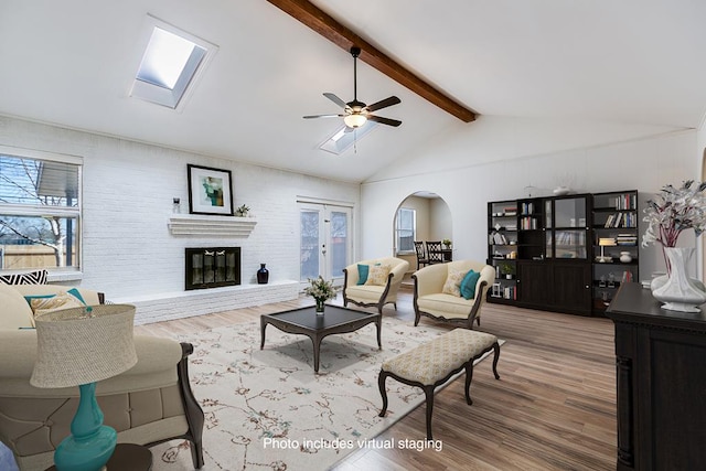 living area with ceiling fan, lofted ceiling with skylight, a fireplace, wood finished floors, and arched walkways