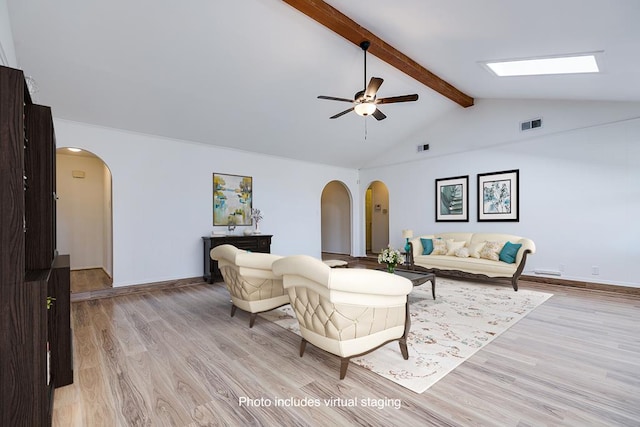 living area featuring arched walkways, beam ceiling, ceiling fan, and light wood finished floors