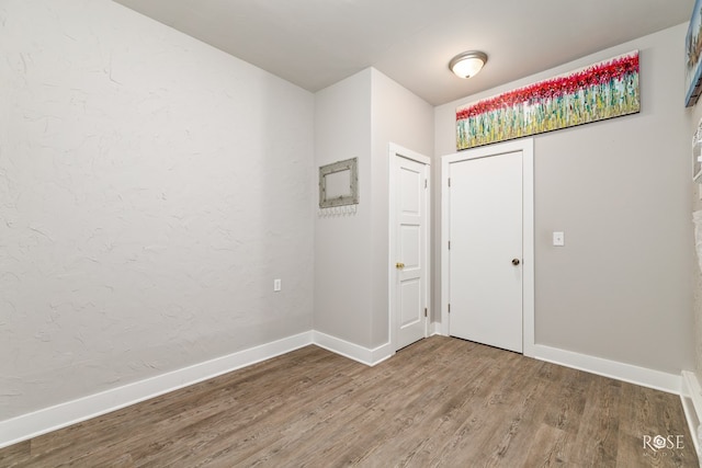 foyer entrance featuring baseboards, wood finished floors, and a textured wall