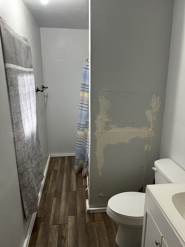 bathroom with wood-type flooring, walk in shower, vanity, and toilet