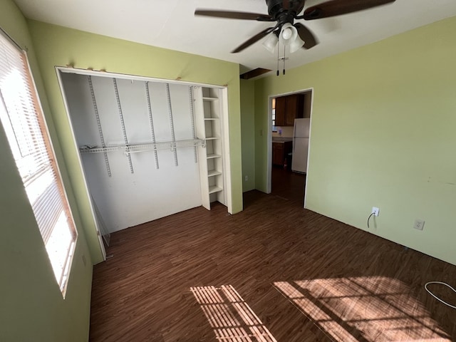 unfurnished bedroom with dark hardwood / wood-style flooring, white fridge, ceiling fan, and a closet