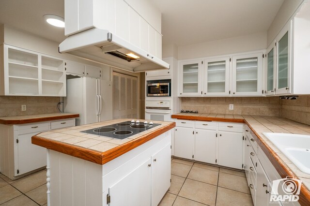 kitchen with white appliances, tile countertops, a kitchen island, and white cabinets