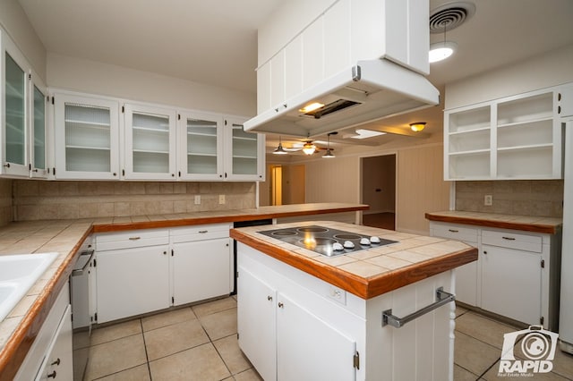 kitchen featuring backsplash, range hood, a center island, tile counters, and white cabinets