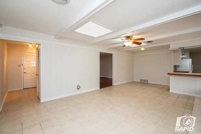 unfurnished living room with beamed ceiling, ceiling fan, a skylight, and light tile patterned floors