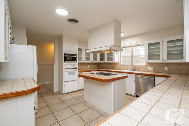 kitchen with appliances with stainless steel finishes, tile counters, a kitchen island, and white cabinets