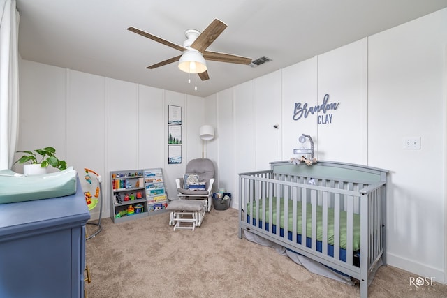 carpeted bedroom with a crib and ceiling fan