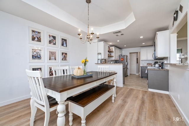 dining area featuring crown molding, a raised ceiling, a chandelier, and light wood-type flooring