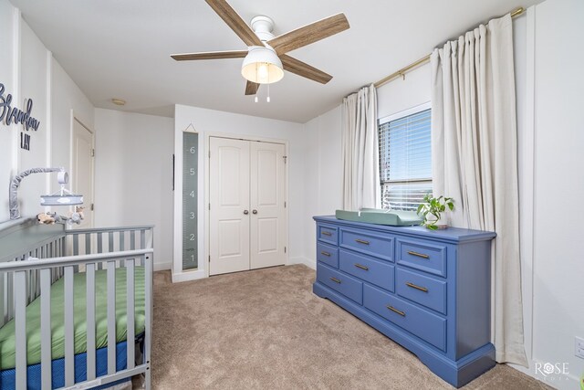 bedroom featuring light carpet, a closet, a nursery area, and ceiling fan