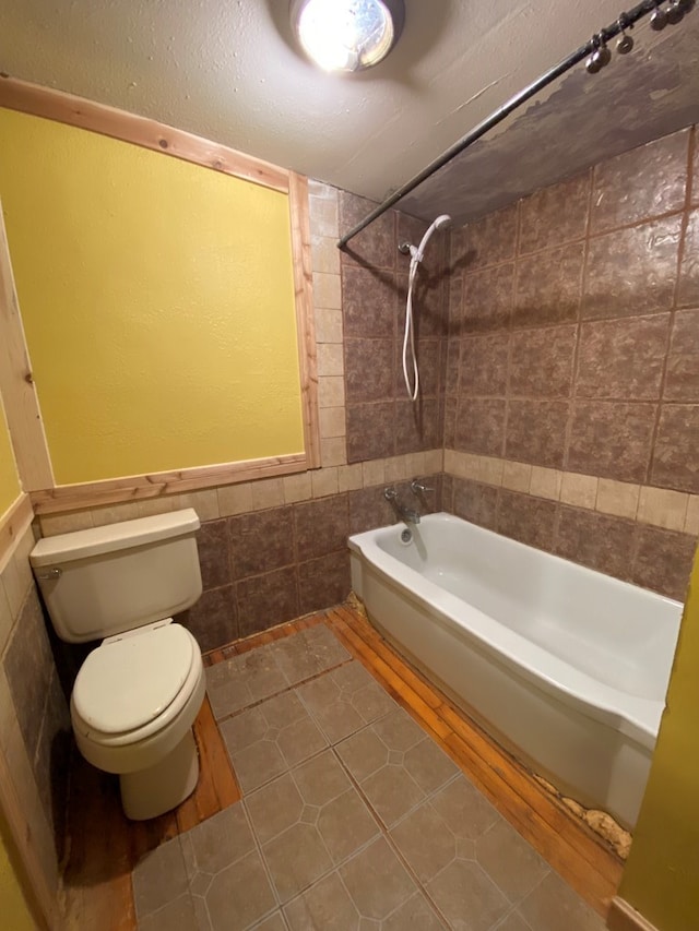 bathroom featuring tile walls, tiled shower / bath, tile patterned floors, and toilet