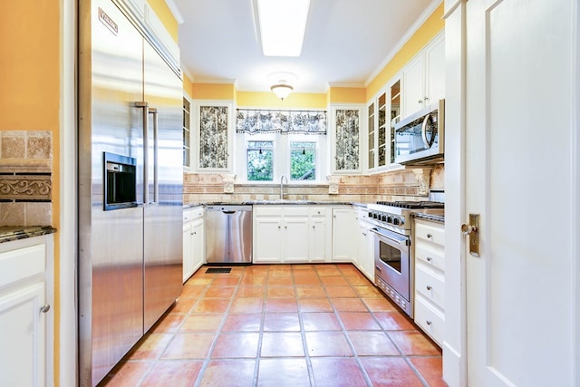 kitchen featuring premium appliances, backsplash, sink, and white cabinets