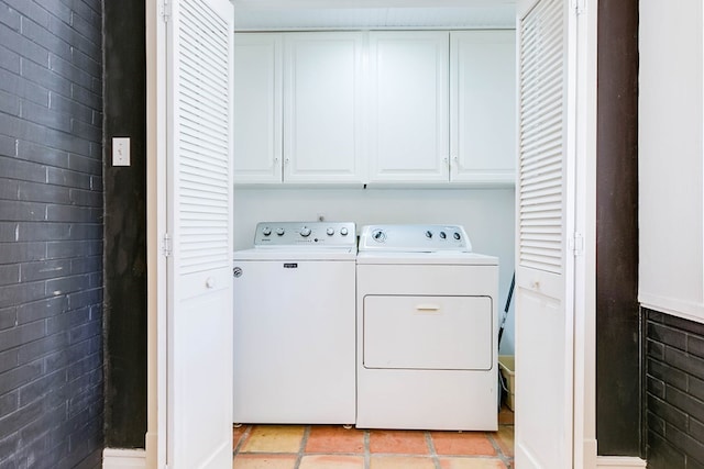 clothes washing area with light tile patterned flooring, washing machine and dryer, cabinets, and brick wall