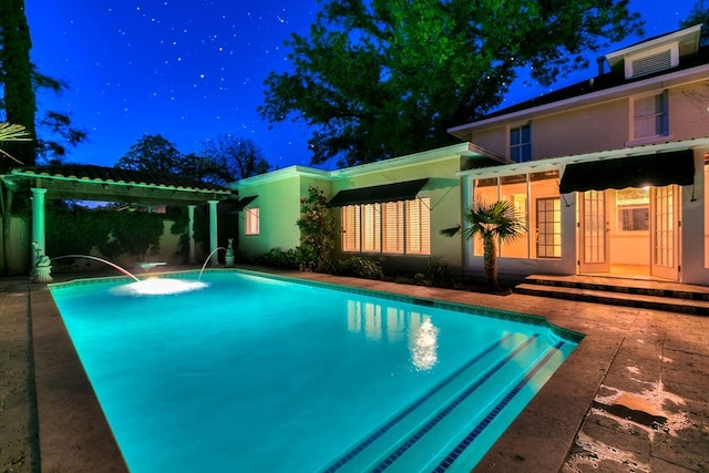 pool at night featuring pool water feature