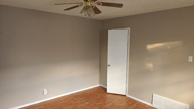 empty room with a ceiling fan, wood finished floors, visible vents, baseboards, and a textured ceiling