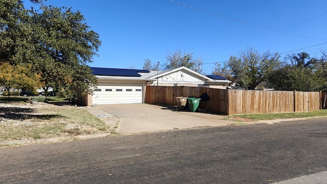 view of front of property featuring solar panels, an attached garage, concrete driveway, and fence