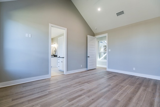 unfurnished bedroom featuring light wood-type flooring, high vaulted ceiling, and ensuite bathroom