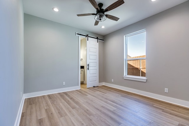 unfurnished bedroom with a barn door, ensuite bath, ceiling fan, and light hardwood / wood-style floors