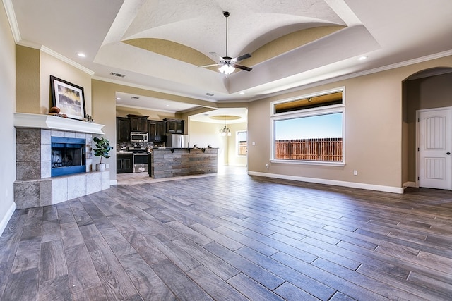 unfurnished living room featuring crown molding, ceiling fan, a tray ceiling, and a fireplace