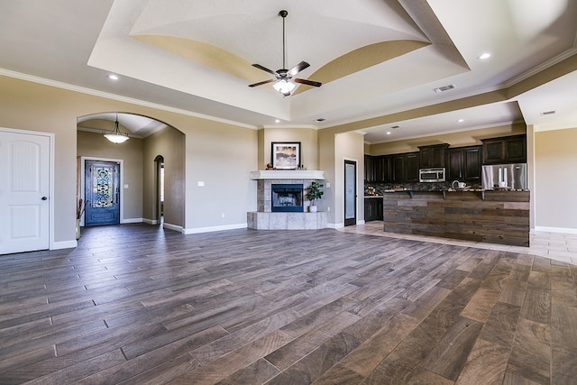 unfurnished living room featuring a fireplace, ornamental molding, a raised ceiling, and ceiling fan