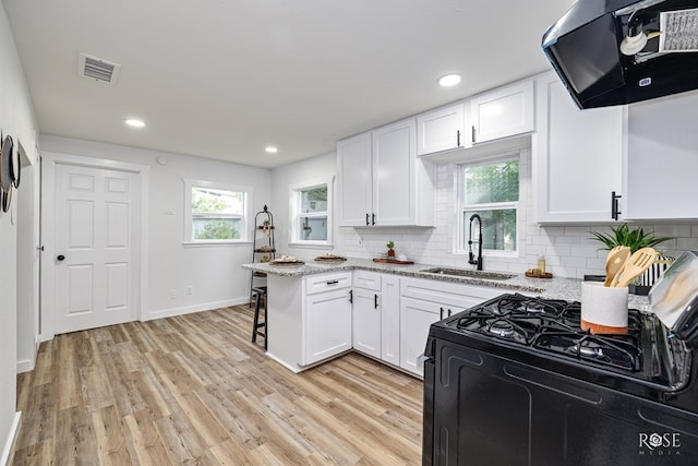 935 E 40th St, San Angelo, TX 76903 - kitchen with ventilation hood, gas stove, white cabinetry, light wood finished floors, and decorative backsplash
