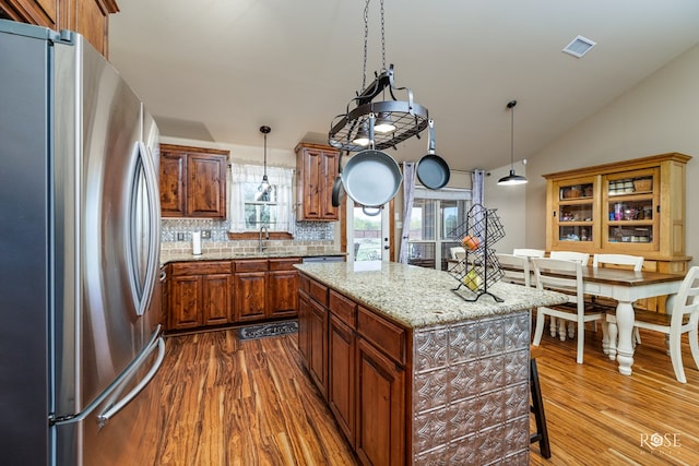 kitchen with stainless steel fridge, hanging light fixtures, a kitchen island, dark hardwood / wood-style flooring, and decorative backsplash