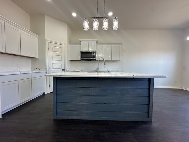 kitchen featuring pendant lighting, sink, white cabinets, a kitchen island with sink, and light stone counters