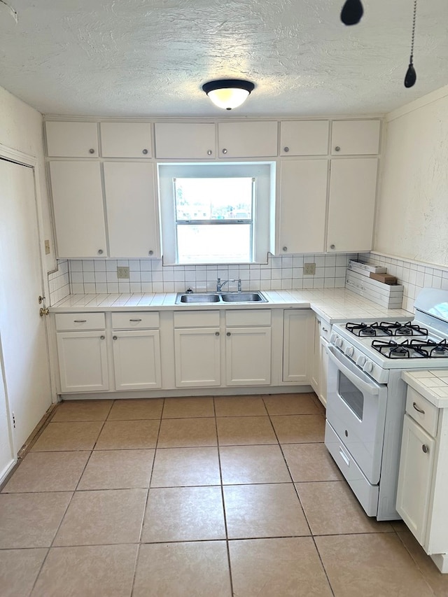 kitchen with white cabinetry, sink, decorative backsplash, and white gas stove