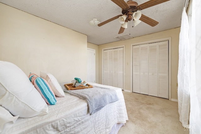 carpeted bedroom with a textured ceiling, ceiling fan, and two closets