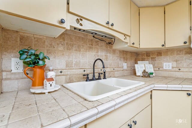 kitchen with tile counters, sink, decorative backsplash, and cream cabinetry