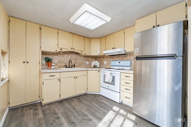 kitchen with white electric range oven, sink, stainless steel fridge, hardwood / wood-style flooring, and cream cabinetry