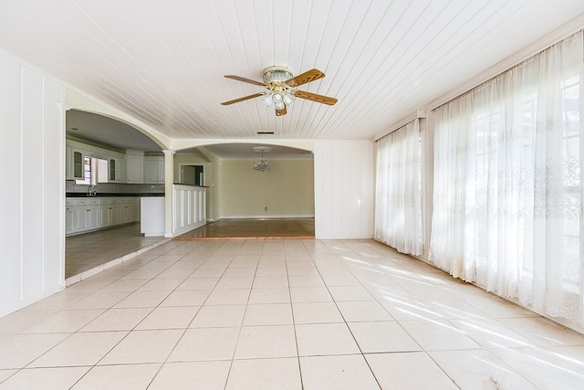 unfurnished room with a wealth of natural light, ceiling fan, arched walkways, and light tile patterned floors